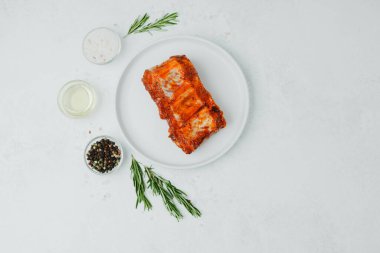 Beyaz tabakta marine edilmiş domuz pirzolası, biberiye ve baharatlı.