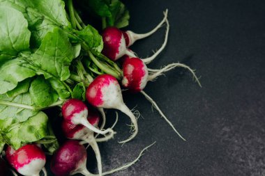 Koyu arkaplanda yeşil yapraklı taze kırmızı turplar.