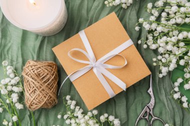 Çiçekler arasında kurdeleli bir hediye kutusu ve yeşil arka planda rahat bir mum.