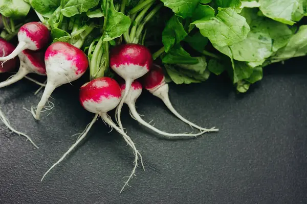 Siyah arka planda yeşil yapraklı taze kırmızı turplar.