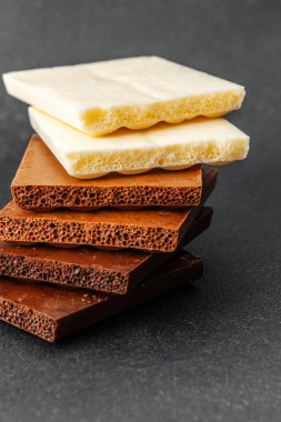 Siyah zemin üzerinde beyaz, süt ve koyu aromalı çeşitli çikolata parçaları yığını