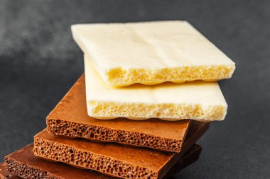 Siyah zemin üzerinde beyaz, süt ve koyu aromalı çeşitli çikolata parçaları yığını