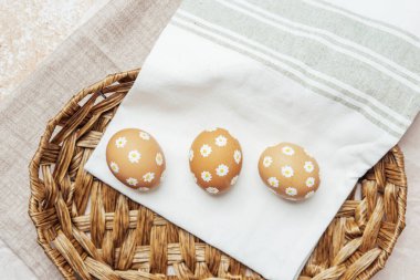Hasır sepetinde papatya çiçekleri olan el yapımı Paskalya yumurtaları. Şenlikli kutlama için kırsal bahar kompozisyonu