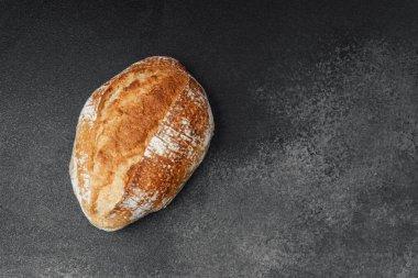 Köy ekmeği, dilimlenmeyi ya da servis edilmeyi bekleyen koyu renkli bir yüzeye dayanır..