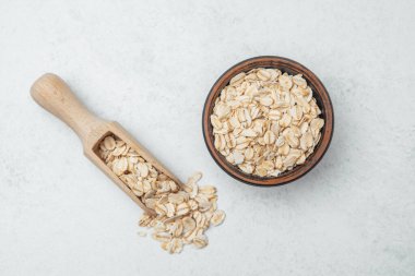 Yulaf dolu bir kase solgun bir yüzeyde tahta bir kepçenin yanında oturur..