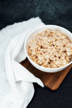 Bir kase pişmiş yulaf ezmesi, tahtanın üzerinde beyaz kumaşın yanında kahvaltıya hazır bekliyor..