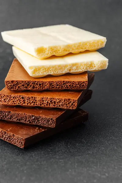 Siyah zemin üzerinde beyaz, süt ve koyu aromalı çeşitli çikolata parçaları yığını