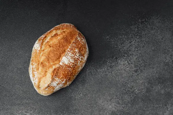 Köy ekmeği, dilimlenmeyi ya da servis edilmeyi bekleyen koyu renkli bir yüzeye dayanır..