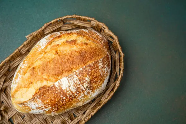 Sıcak bir somun ekşi ekmek yeşil bir masada kırsal bir sepette duruyor..