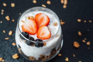 Yoğurtlu granola parfe, koyu arkaplanda çilek ve yabanmersini.
