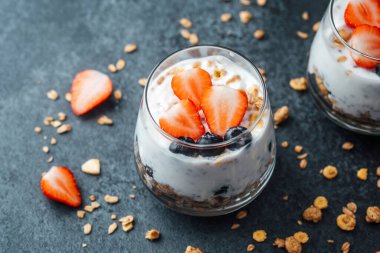 Yoğurtlu granola parfe, koyu arkaplanda çilek ve yabanmersini.