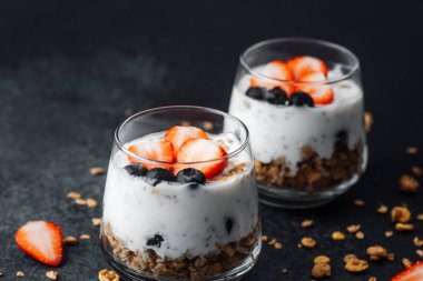Yoğurtlu granola parfe, koyu arkaplanda çilek ve yabanmersini.