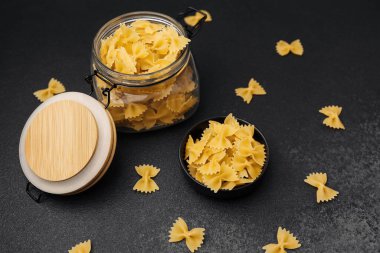 Cam bir kavanoza konmuş Farfalle makarnası ve karanlık bir mutfak tezgahında küçük bir kase..