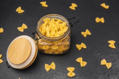 Gevşek parçalarla çevrili pişmemiş farfalle makarnasıyla dolu cam bir kavanoz..