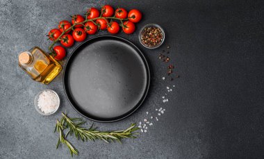 Boş siyah tabak, kirazlı domates zeytinyağı biberiye tuzu ve siyah arka planda biber.