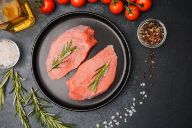 Siyah seramik tabakta çiğ biftek, biberiye, kiraz, domates, tuz ve biber.