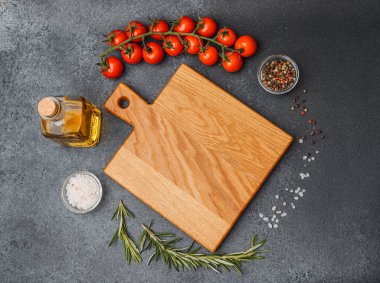 Boş ahşap kesme tahtası, kiraz domatesli zeytinyağı, tuz biberi ve koyu arkaplanda biberiye.