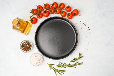 Domates, biberiye, tuz, yağ ve biber içeren yemek malzemelerinin olduğu boş siyah tabağın üst görüntüsü