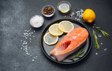 Taze somon filetosu limon dilimleri, otlar ve baharatlarla dolu bir tabakta duruyor..