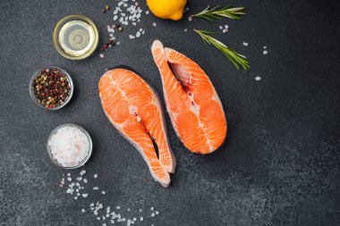 Somon biftekleri siyah bir tezgahta otlar, limonlar ve baharatlarla sıralanır..