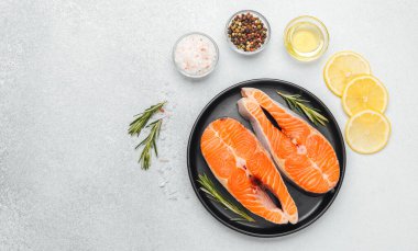 Bir tabakta iki somon fileto ve yanında otlar, baharatlar ve limon dilimleri..