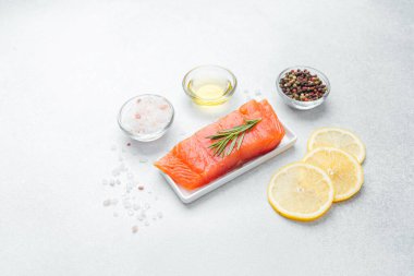 Biberiye, tuz, limon dilimleri ve biberle süslenmiş somon filetosu pişirmeye hazır..