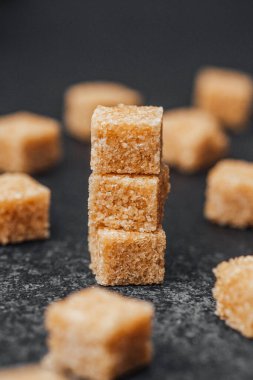 Koyu bir yüzeye yığılmış kahverengi şeker küpleri ve yanında ilave küpler..