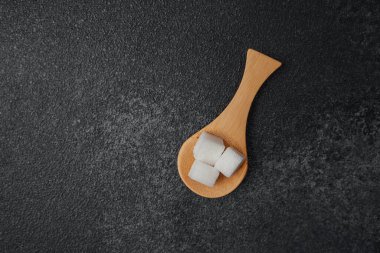 Şeker küpleri, siyah bir arka planda tahta bir kaşığa yerleştirilmiş..