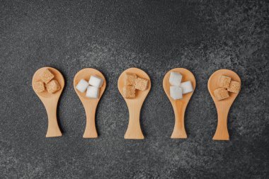 Farklı şeker tipleri koyu bir yüzeyde tahta kaşıklarda sergilenir..