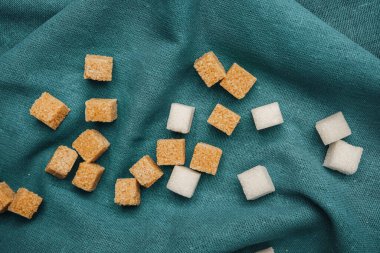 Kahverengi ve beyaz şeker küpleri artistik olarak gümüş rengi kumaş üzerine dizilmiştir..