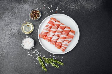 Çiğ domuz pastırması beyaz tabağa sarılmış, baharatlı ve otlu.