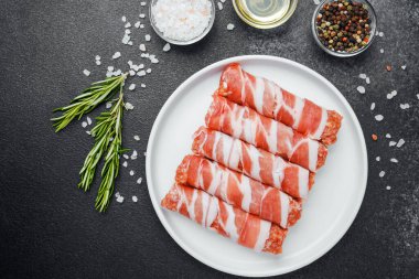 Çiğ domuz pastırması beyaz tabağa sarılmış, baharatlı ve otlu.