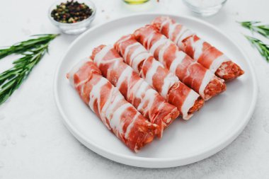 Jambona sarılmış sosis, beyaz tabakta otlar ve yağla birlikte.