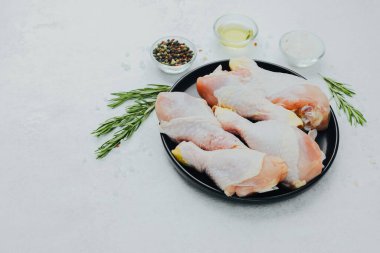 Biberiye ve baharatlı siyah tabakta çiğ tavuk budu.