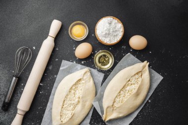 Malzemelerin üst görüntüsü ve iki pişmemiş khachapuri un kaplı siyah masa üzerinde
