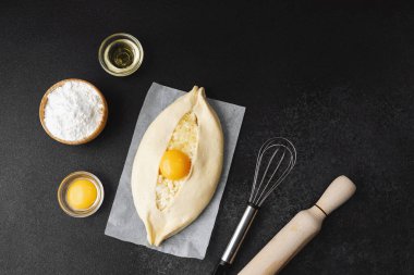 Parşömen üzerinde peynir ve sarısı olan Khachapuri ve koyu mutfak masası.