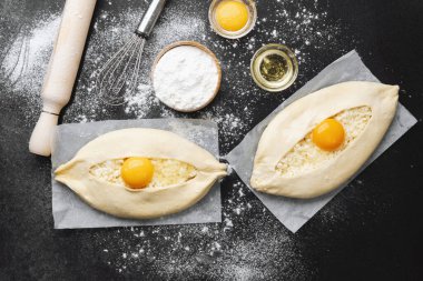 Un kaplı yüzeyinde yumurta sarısı olan iki çiğ khachapuri.