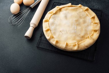 Yuvarlak bir hamur işi serinletici rafta duruyor yanında da yumurta ve çırpma teli var..