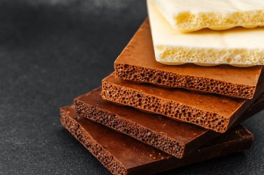 Siyah zemin üzerinde beyaz, süt ve koyu aromalı çeşitli çikolata parçaları yığını