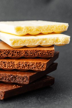 Siyah zemin üzerinde beyaz, süt ve koyu aromalı çeşitli çikolata parçaları yığını