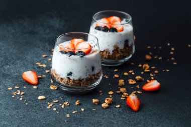 Yoğurtlu granola parfe, koyu arkaplanda çilek ve yabanmersini.