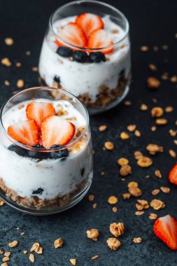 Yoğurtlu granola parfe, koyu arkaplanda çilek ve yabanmersini.