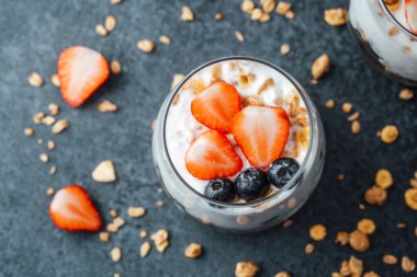 Yoğurtlu granola parfe, koyu arkaplanda çilek ve yabanmersini.