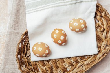 Hasır sepetinde papatya çiçekleri olan el yapımı Paskalya yumurtaları. Şenlikli kutlama için kırsal bahar kompozisyonu.