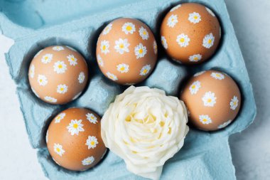 El boyaması Paskalya yumurtaları, papatya desenli beyaz güllü mavi bir karton. Işık arkaplanındaki Paskalya kompozisyonu