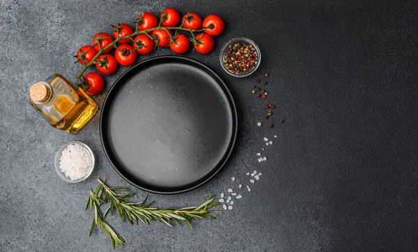 Boş siyah tabak, kirazlı domates zeytinyağı biberiye tuzu ve siyah arka planda biber.