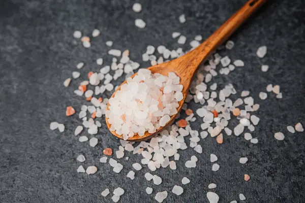 Ahşap kaşık pembe himalaya tuzu ve dokulu siyah yüzey.