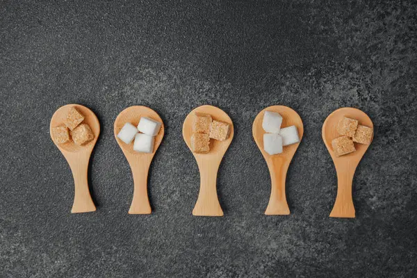 Farklı şeker tipleri koyu bir yüzeyde tahta kaşıklarda sergilenir..