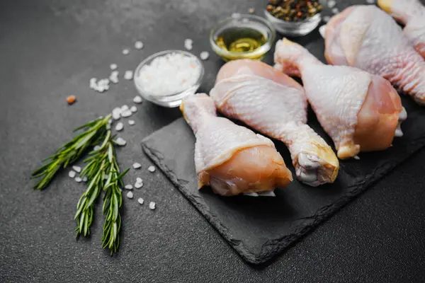 Siyah tahta üzerine yerleştirilmiş tavuk budu, otlar ve tuzlu.