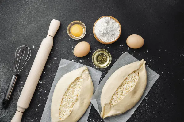 Malzemelerin üst görüntüsü ve iki pişmemiş khachapuri un kaplı siyah masa üzerinde